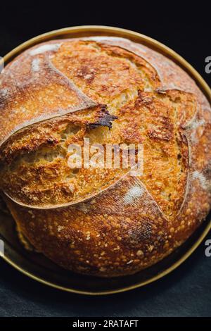 gros plan de boule de levain assis soigneusement dans le plateau rond en laiton sur le noir Banque D'Images