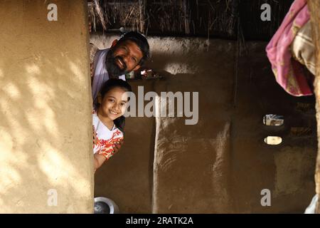 Heureux père indien et fille jouant à cache-cache. Père célibataire avec sa fille qui regarde joyeusement hors de leur chalet dans l'Inde rurale. Banque D'Images