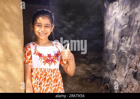 Heureuse fille indienne rurale debout sur sa porte de chalet portant une robe, souriant et regardant dans la caméra en été de jour. Levez-vous avec le sourire. Banque D'Images