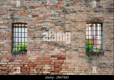 Vieux mur de briques rouges avec deux fenêtres grillées en fer rouillé. Banque D'Images