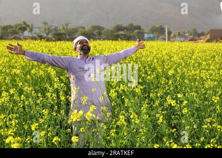 Portrait d'un fermier indien heureux sentant le vent tout en se tenant dans le champ étirant ses bras. Inde rurale. Joyeux Villager pour voir les cultures florissantes. Banque D'Images