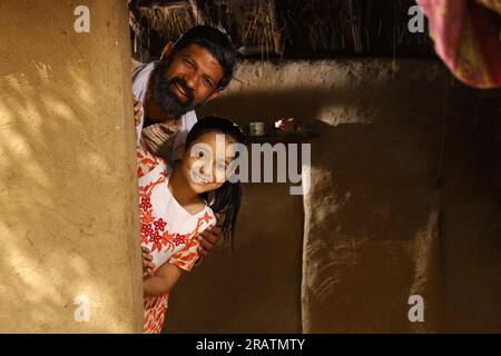 Heureux père indien et fille jouant à cache-cache. Père célibataire avec sa fille qui regarde joyeusement hors de leur chalet dans l'Inde rurale. Banque D'Images