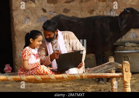 Père et fille surfant ensemble sur un ordinateur portable dans un village rural indien profitant de toilettage numérique de l'Inde et se concentrant sur l'ère numérique assis à l'extérieur Banque D'Images