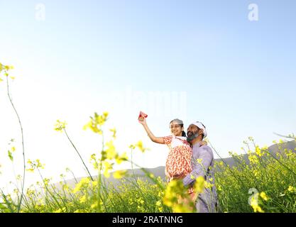 Agriculteurs ruraux indiens heureux. Père et fille dans le champ de moutarde jouant avec des avions en papier. Fille rêve de voler à l'étranger. Hôtesse de l'air. Banque D'Images