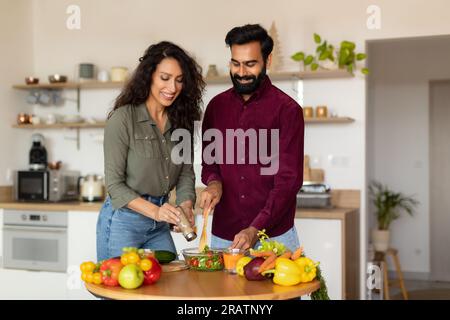 Heureux époux arabes aimant faire de la salade de légumes sains ensemble, homme aidant sa femme, intérieur de la cuisine, espace de copie Banque D'Images