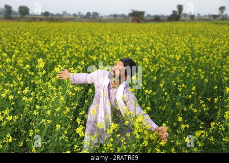 Portrait d'un fermier indien heureux sentant le vent tout en se tenant dans le champ étirant ses bras. Inde rurale. Joyeux Villager pour voir les cultures florissantes. Banque D'Images