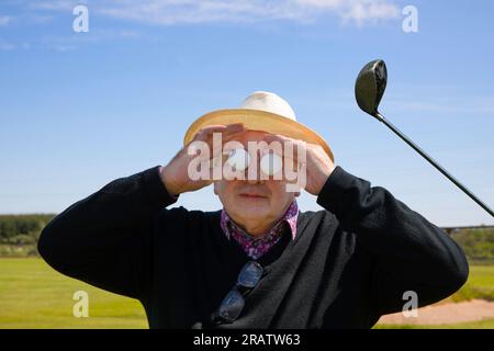 L'homme âgé tient des balles de golf devant ses yeux sur le fond d'un terrain de golf et d'un club de golf. Concept de golf fou, fou de golf ou aller Banque D'Images