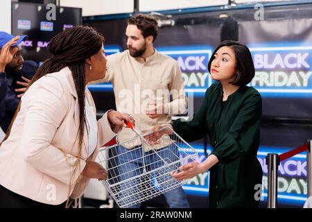 Black Friday chaos. Les acheteurs de gens se comportent grossièrement et agressifs lors de leurs achats pendant les soldes, se battent entre les chasseurs de bonnes affaires. Deux femmes émotionnelles en colère qui se battent pour un panier Banque D'Images