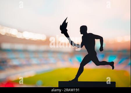 Symbole de l'unité : silhouette de l'athlète portant le relais de la flamme contre le stade moderne d'athlétisme. Une photo captivante pour le Summer Game 20 Banque D'Images