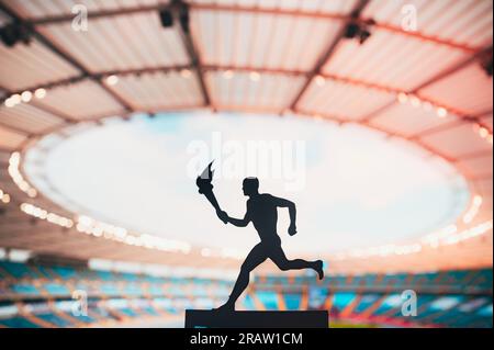 Silhouette de l'athlète tenant le relais de la flamme, face à un stade moderne d'athlétisme. Capturer l'esprit de l'événement d'été 2024 à Paris Banque D'Images