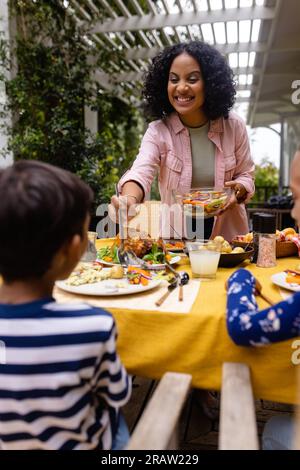 Heureux parents biracial, fils et fille servant de la nourriture et assis à la table dans le jardin, espace de copie. Été, famille, unité, nourriture et style de vie, onu Banque D'Images