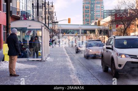 Winnipeg, Manitoba, Canada - 11 17 2014 : vue hivernale le long de l'avenue Portage avec des gens se cachant du vent froid dans les abris en verre d'un arrêt d'autobus Banque D'Images