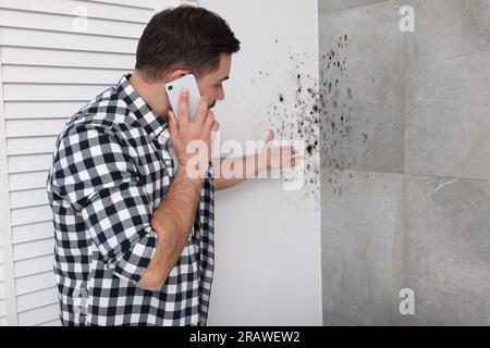 Service de démoulage. Homme parlant au téléphone et regardant les murs affectés dans la chambre Banque D'Images