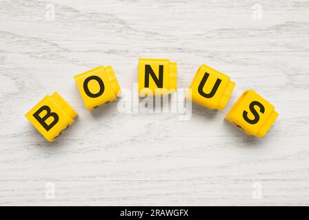 Mot Bonus fait de cubes jaunes avec des lettres sur fond en bois blanc, vue de dessus Banque D'Images