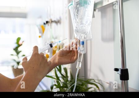 Gros plan des mains d'un médecin caucasien tenant la seringue et le goutte à goutte à l'hôpital. Services hospitaliers, médicaux et de soins de santé, inchangés. Banque D'Images