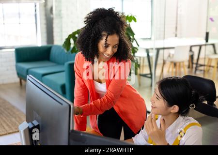 Heureux divers collègues d'affaires occasionnels féminins utilisant l'ordinateur discutant du travail au bureau dans le bureau. Travail d'équipe, travail, affaires, communication et occasionnel o Banque D'Images