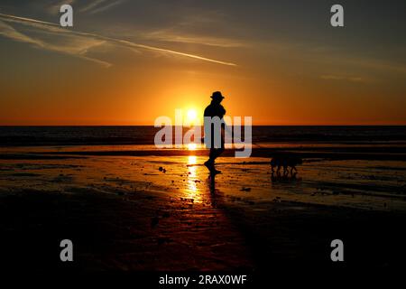 Un homme emmène son chien pour un troll au coucher du soleil sur la plage de Malibu lors d'un coucher de soleil incroyable du sud de la californie. Banque D'Images