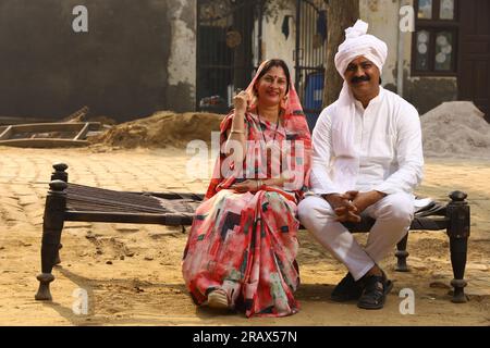 Heureuse famille indienne rurale dans le village. Mari, femme assis sur un lit bébé devant leur maison dans la cour avant. homme en pyjama kurta et femme portant saree, sari Banque D'Images