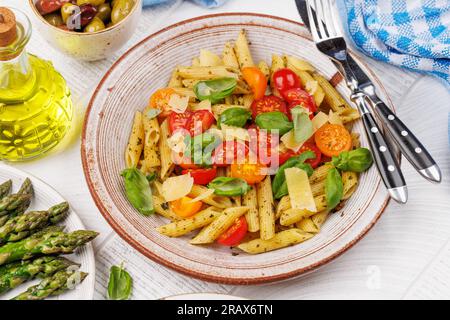 Une délicieuse assiette de pâtes italiennes ornée de tomates fraîches et de feuilles de basilic aromatiques, d'asperges grillées et de crevettes Banque D'Images