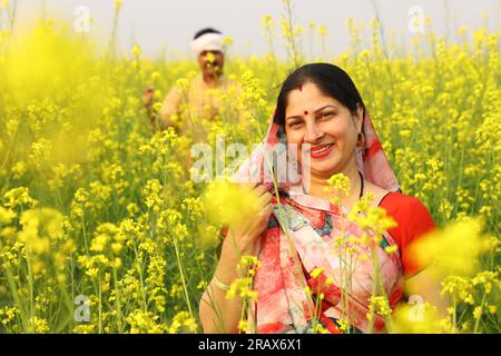 Famille indienne rurale debout dans le champ de moutarde et mari et femme sont heureux de voir les avantages agricoles du champ. Banque D'Images