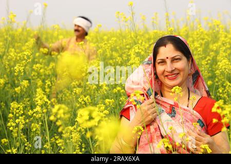 Famille indienne rurale debout dans le champ de moutarde et mari et femme sont heureux de voir les avantages agricoles du champ. Banque D'Images