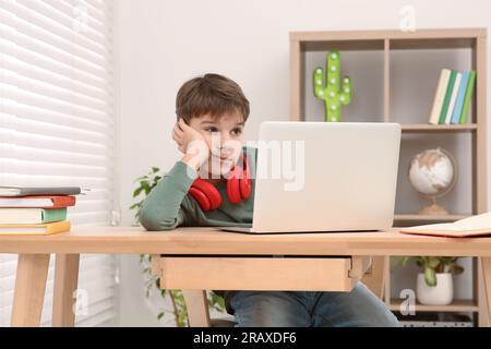 Garçon fatigué avec casque rouge utilisant un ordinateur portable au bureau dans la chambre. Lieu de travail à domicile Banque D'Images