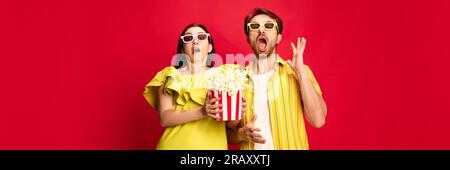 Homme et femme regardant émotionnellement un film, mangeant du pop-corn sur fond de studio rouge. Film d'horreur Banque D'Images