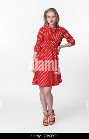 Jeune femme blonde avec les cheveux longs habillée en robe à pois rouge d'été, chaussures rouges debout en pleine longueur et pose sur fond blanc Banque D'Images