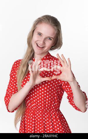 Portrait de jeune femme blonde confesse dans l'amour, fait le geste de coeur avec les deux mains et regardant la caméra, montrant des sentiments vrais sur fond blanc Banque D'Images