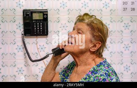 femme adulte mature parlant au téléphone dans une cuisine avec un style rétro. Femme âgée avec téléphone dans le fond vintage Banque D'Images