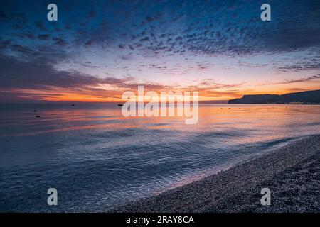 beauté à couper le souffle de la nature comme des teintes vibrantes peignent le ciel lors d'un lever de soleil envoûtant sur la plage de la mer Banque D'Images