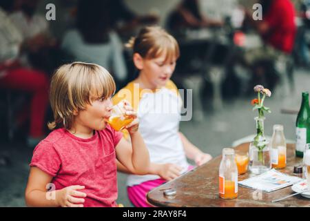 Groupe de deux enfants drôles prenant un verre dans le café, à l'extérieur Banque D'Images