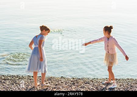 Deux mignonnes petites filles préadolescentes jouant au bord du lac par une belle journée ensoleillée, portant des robes de fête Banque D'Images