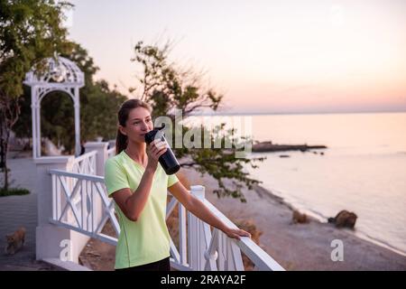 Portrait d'un athlète qui boit de l'eau dans une bouteille de sport. Une jeune femme étanche sa soif avec un buveur de forme physique. Maintien de l'équilibre de l'eau duri Banque D'Images