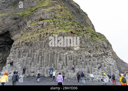 Plage de sable noir de Reynisfjara, Islande - 06.22.2023 : personnes grimpant sur des colonnes de basalte sur la plage de Reynisfjara Banque D'Images