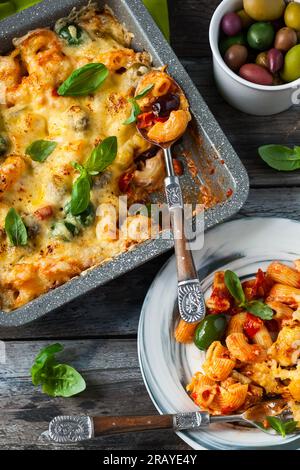 Pâtes cuites au four avec olives colorées, poivrons et tomates. Gratin de pâtes et légumes dans un plat allant au four Banque D'Images