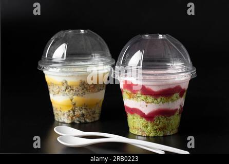 Gâteaux à emporter dans des verres avec pistaches, mousse de fraise, biscuit aux graines de pavot et caillé de citron sur fond noir Banque D'Images