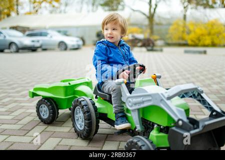 Adorable garçon en bas âge chevauchant son tracteur jouet dans une ville sur la soirée ensoleillée d'automne. Jeune enfant roulant sur un rouleau. Loisirs actifs et sports de plein air pour les enfants Banque D'Images