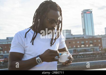 Jeune homme africain avec des dreadlocks et un bon style profiter de manger de la crème glacée au coucher du soleil à Buenos Aires, concept de gens, espace de copie Banque D'Images