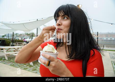 jeune femme latine heureuse en plein air mangeant de la crème glacée, tenant une petite tasse avec des saveurs mélangées. espace de copie Banque D'Images