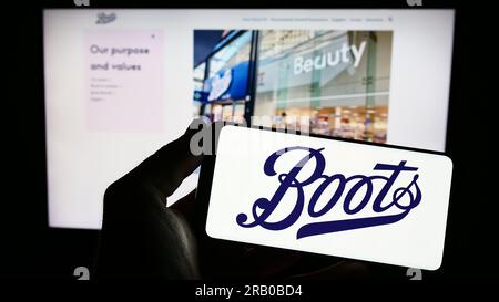 Personne tenant le smartphone avec le logo de la société pharmaceutique britannique Boots UK Limited sur l'écran en face du site Web. Concentrez-vous sur l'affichage du téléphone. Banque D'Images