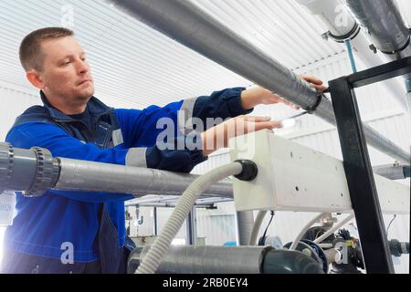 Serrurier professionnel vérifie les tuyaux et l'approvisionnement en eau à l'intérieur du bâtiment industriel. Vrai travailleur. Flux de travail authentique. Banque D'Images