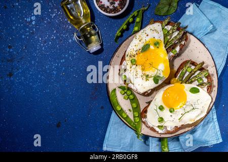Savoureux sandwichs de petit déjeuner, pain grillé avec fromage à la crème, asperges et œufs au plat, avec pois verts, huile d'olive et épices, vue de dessus espace copie Banque D'Images