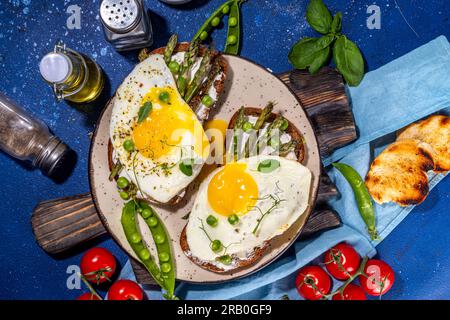 Savoureux sandwichs de petit déjeuner, pain grillé avec fromage à la crème, asperges et œufs au plat, avec pois verts, huile d'olive et épices, vue de dessus espace copie Banque D'Images