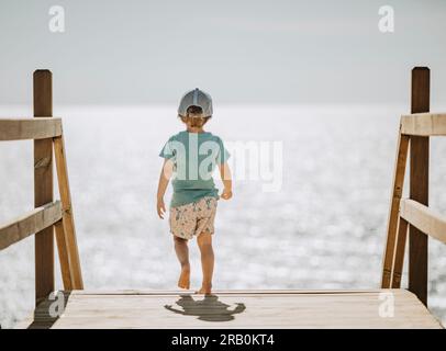 Petit garçon sur les escaliers en bois au bord de la mer Banque D'Images