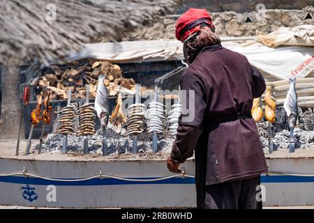 Un chef cuisinant du poisson, des sardines et du bar, sur des brochettes autour d'un barbecue au feu de bois en plein air. Le barbecue, dans un bateau, est sur la plage de la Costa Del sol Banque D'Images