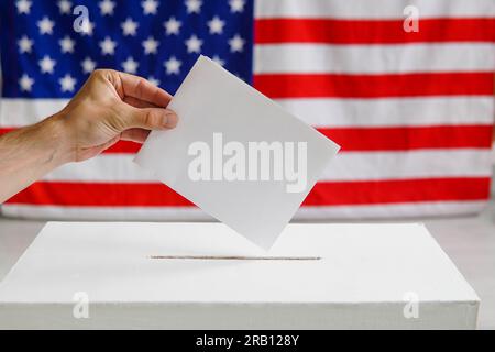 Homme mettant un bulletin de vote dans une boîte de vote. USA drapeau américain sur le fond. Banque D'Images