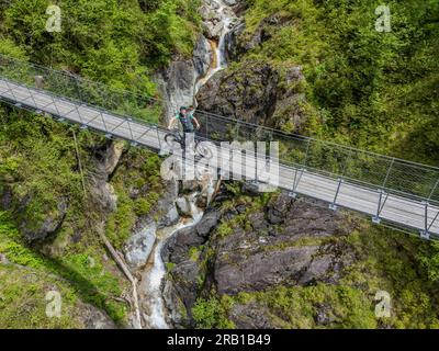 Italie, Trentin, province de trente, cycliste avec e-vtt sur le pont tibétain suspendu au-dessus du Rio de la Vecia le long de la piste cyclable Primiero San Martino di Castrozza, Dolomites Banque D'Images