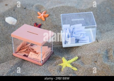 Les urnes pour les élections au congrès et au sénat avec les votes des citoyens sur le sable de la plage en été Banque D'Images