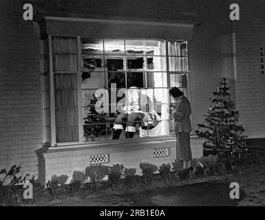 Beverly Hills, Californie : 22 décembre 1949. Cette résidente de Beverly Hills met la touche finale à sa décoration de fenêtre de Noël du Père Noël endormi dans une chaise. Banque D'Images